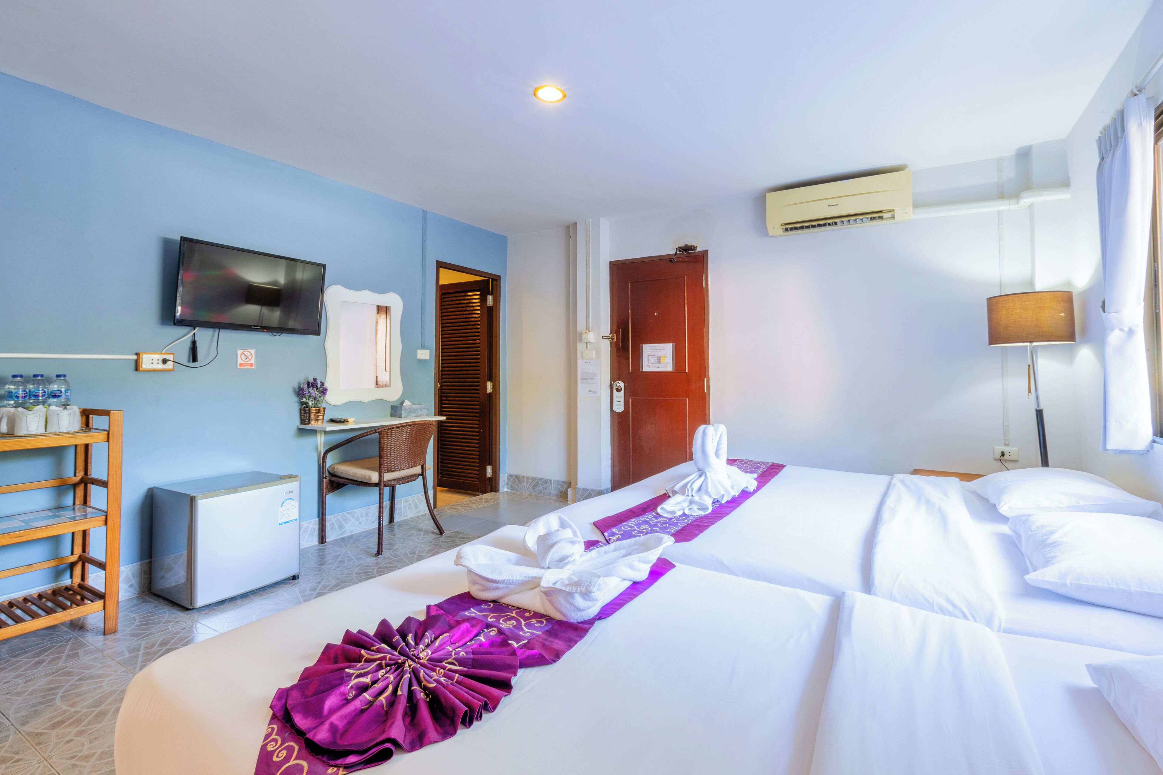 A hotel room with a bed, a desk, a TV, a refrigerator, and a chair.