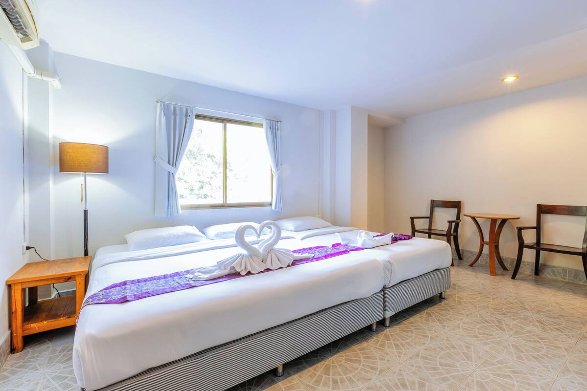 A hotel room with a large bed, two chairs, a small table, and a window with curtains.