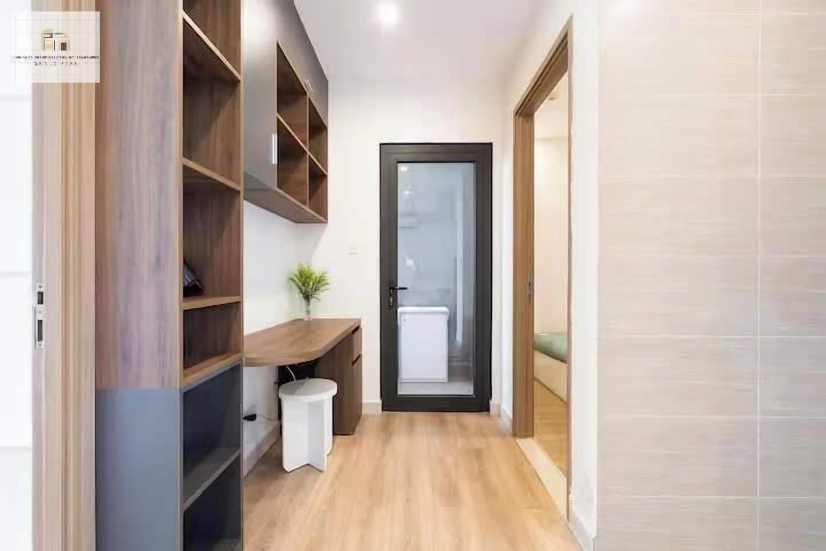A narrow hallway with wooden shelving, a small white stool, and a door leading to a room with a radiator.