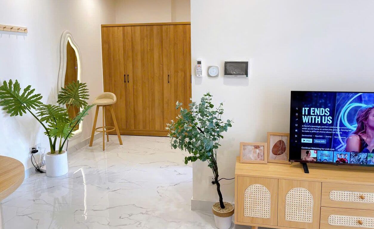 A modern living room with a wooden cabinet, a television displaying a movie, and two potted plants.