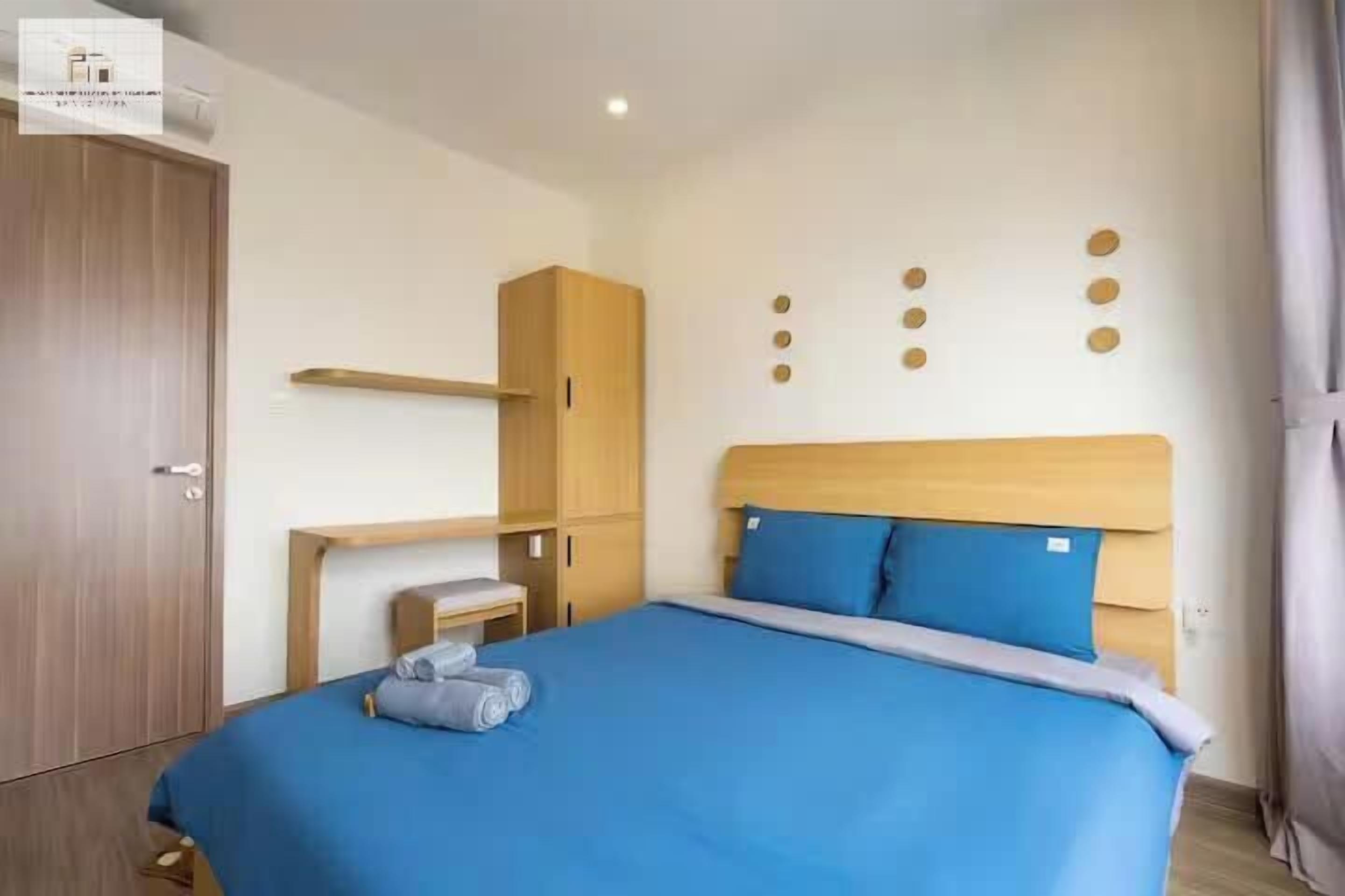 A hotel room with a bed, wooden wardrobe, and a small table with a lamp.