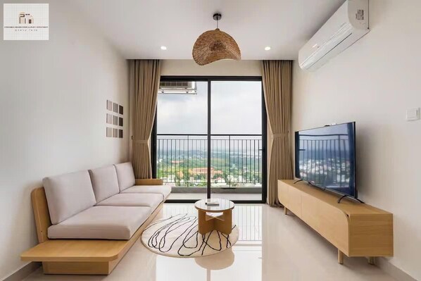 Una sala de estar moderna con un sofá, una mesa de centro, un televisor sobre un mueble de madera y un ventanal con vistas.