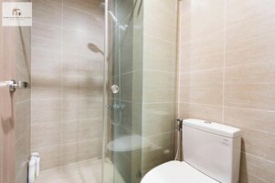 A modern bathroom with a glass-enclosed shower, a toilet, and a wall-mounted soap dispenser.