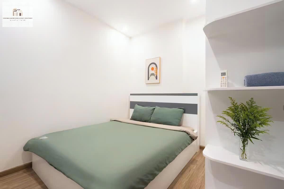Een keurig opgemaakt slaapkamer met een bed, een nachtkastje met een bloemenvaas en een kunstwerk aan de muur.