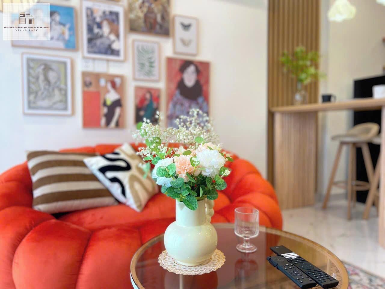 A living room with a red sofa, a white vase with flowers, a glass table, and framed artwork on the wall.