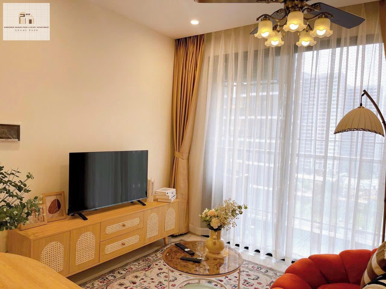 A modern living room with a flat-screen TV on a wooden console, a glass coffee table with a vase, and a red sofa.