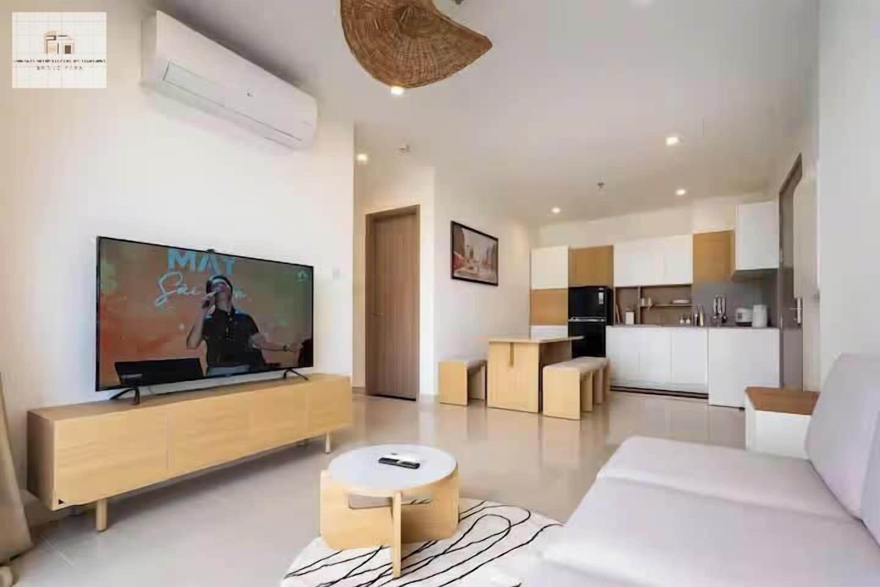 Ein modernes Wohnzimmer mit Flachbildfernseher, einer Couch, einem runden Couchtisch und einer Küche im Hintergrund.