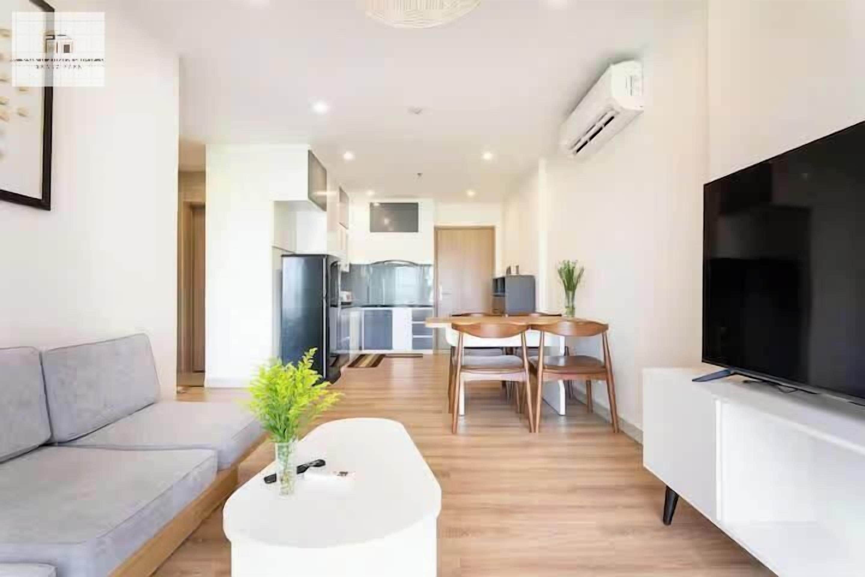A modern living room with a sofa, a coffee table with a plant, a TV on a stand, and a dining area with a table and chairs.