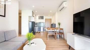 A modern living room with a sofa, a coffee table with a plant, a TV on a stand, and a dining area with a table and chairs.