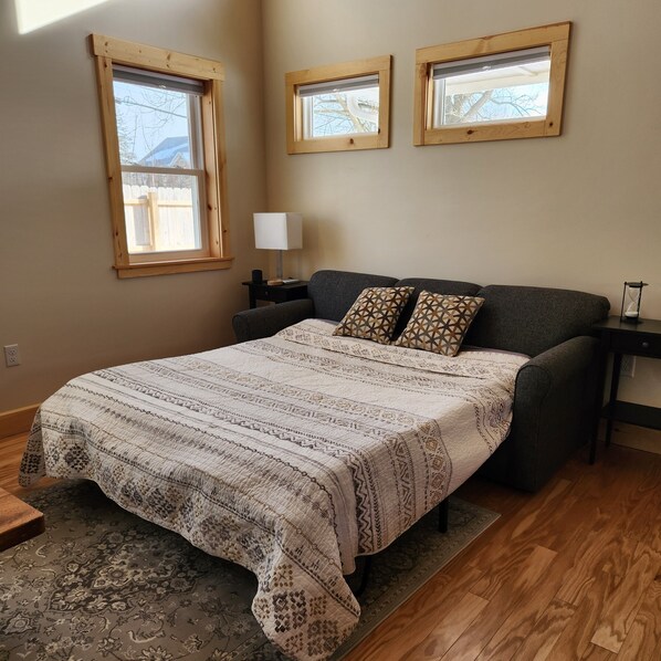 A bedroom with a large bed, two windows, a nightstand, a lamp, and a rug.