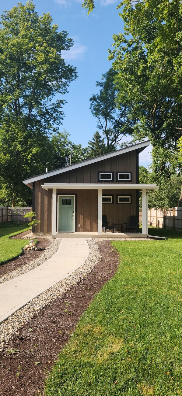 Une maison moderne à deux étages, dotée d’un patio couvert, d’une porte d’entrée et d’un petit jardin.