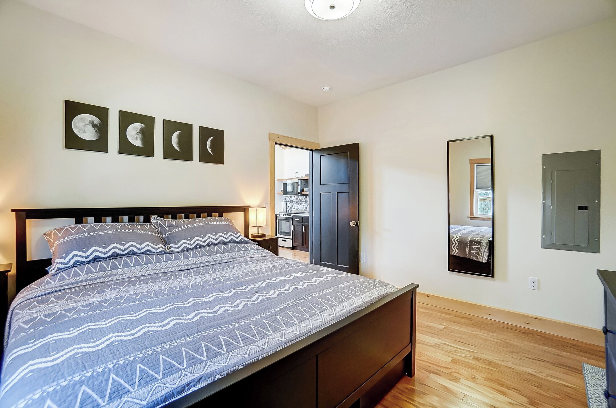 A bedroom with a bed, a door, a mirror, and a wall with framed pictures.