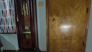 Una habitación con una puerta de madera, un reloj grande y una alfombra estampada con motivos florales.
