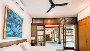A hotel room with a large bed, a ceiling fan, a painting of butterflies, and a view of the outdoor area through glass doors. - Villa Uma Pertiwi by Nakula (Seminyak)