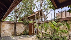 A stone wall with a wooden gate, a paved pathway with stepping stones, and lush greenery. - Villa Uma Pertiwi by Nakula (Seminyak)