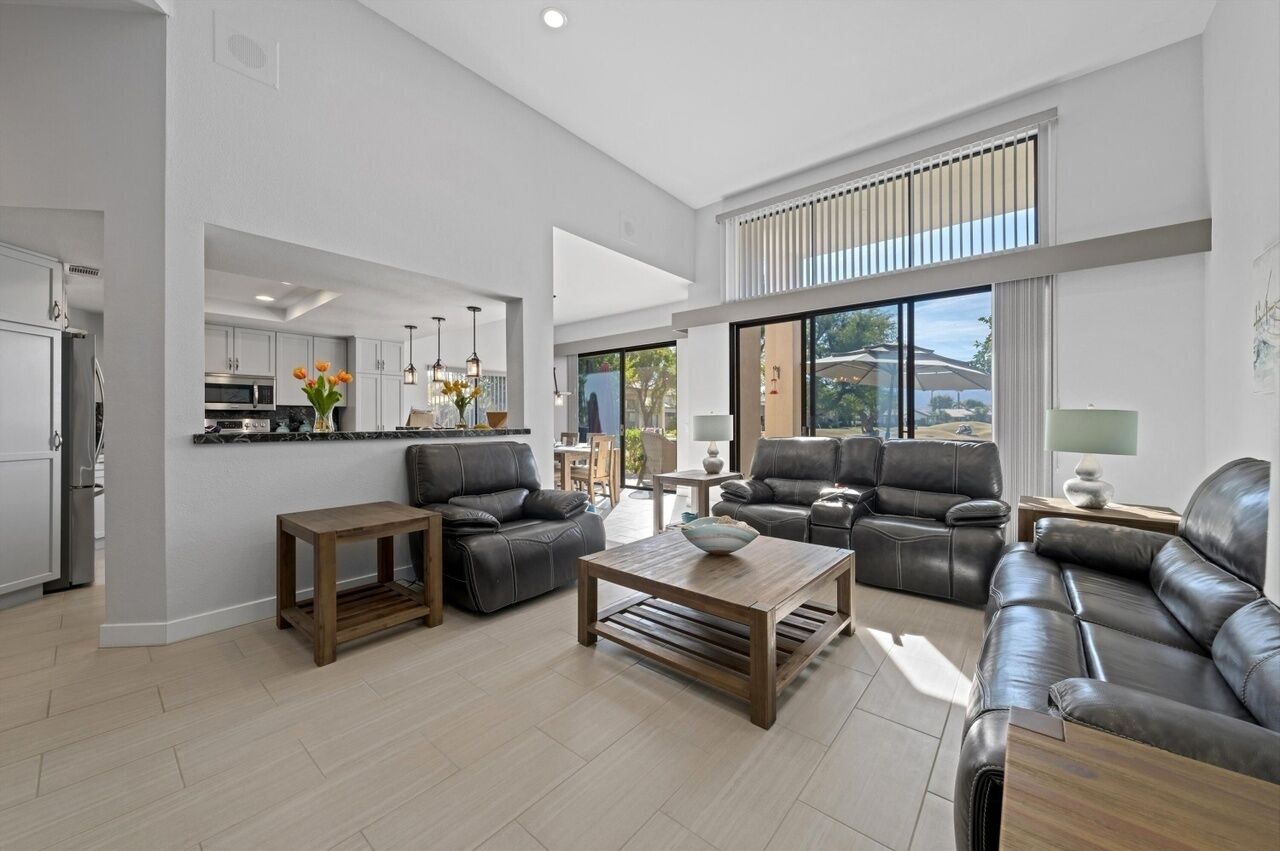 A spacious living area with a modern kitchen, leather sofas, and a large window providing a view of the outdoors.
