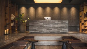 A reception area with a modern design, featuring a stone-textured counter, wooden bookshelves, and a potted plant. - iSuite by Ekosistem (Keroboken Kelod)