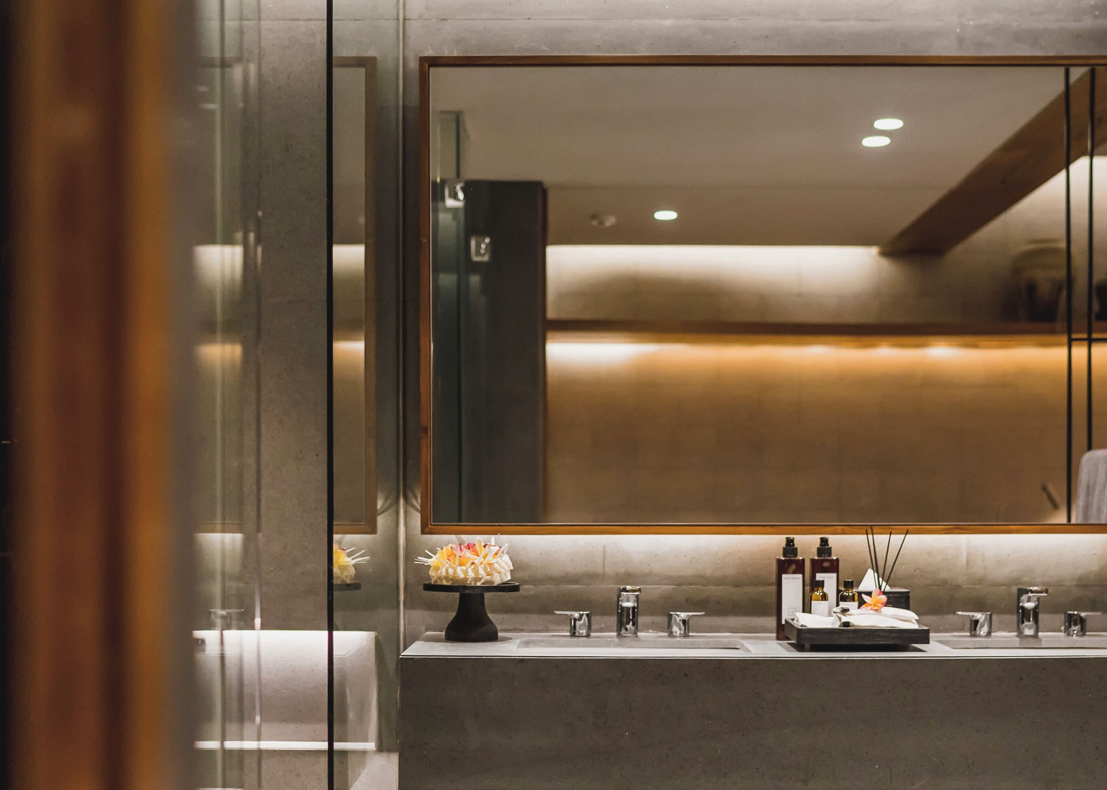 A modern bathroom with a large mirror, a sink with multiple faucets, and a decorative vase.