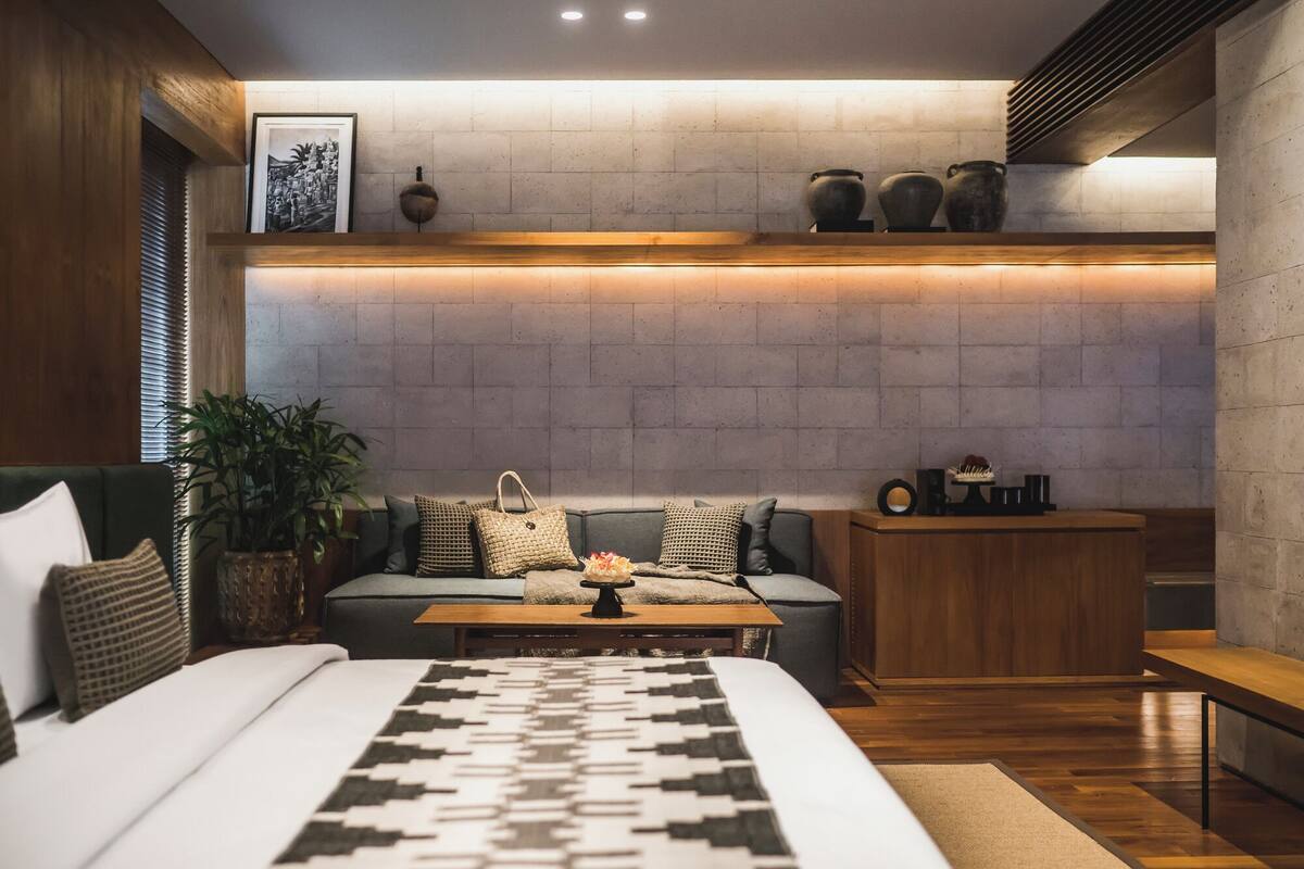 Un dormitorio moderno con cama, sofá, mesa de centro y una mesita de noche de madera.