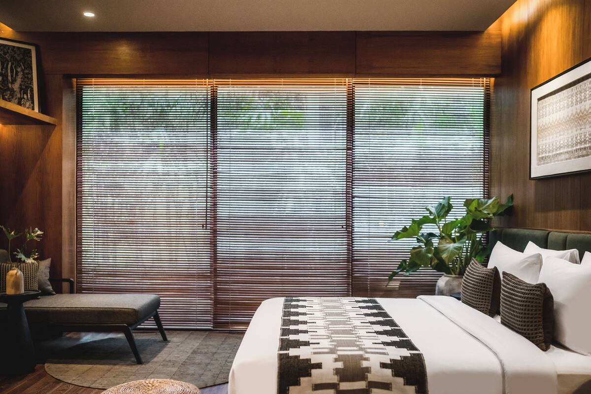 Un dormitorio con una cama grande, una mesita de noche, una silla y una ventana con persianas.