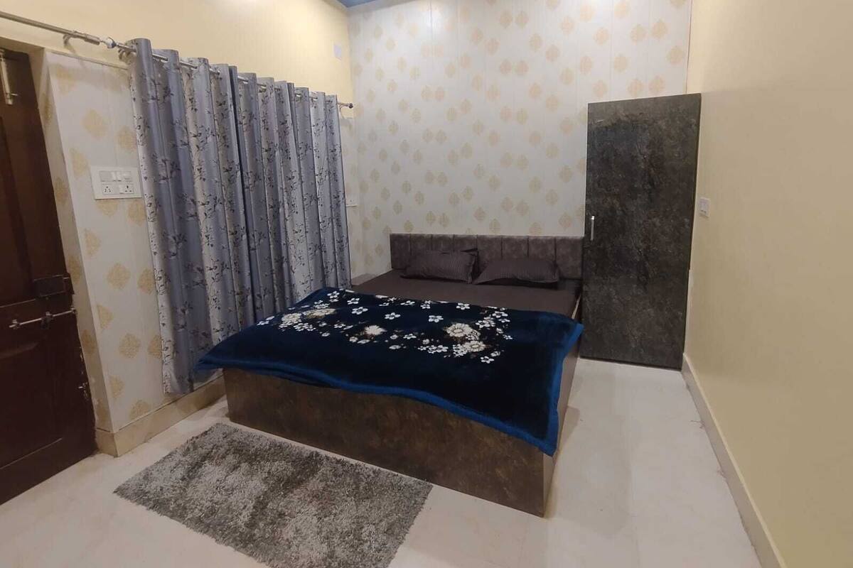 A bedroom with a bed, a dark-colored wardrobe, a patterned curtain, and a patterned wall.