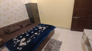 Une chambre à coucher avec un lit, une couvre-lit à motifs floraux bleu foncé, un tapis gris, un canapé marron et une armoire en bois.