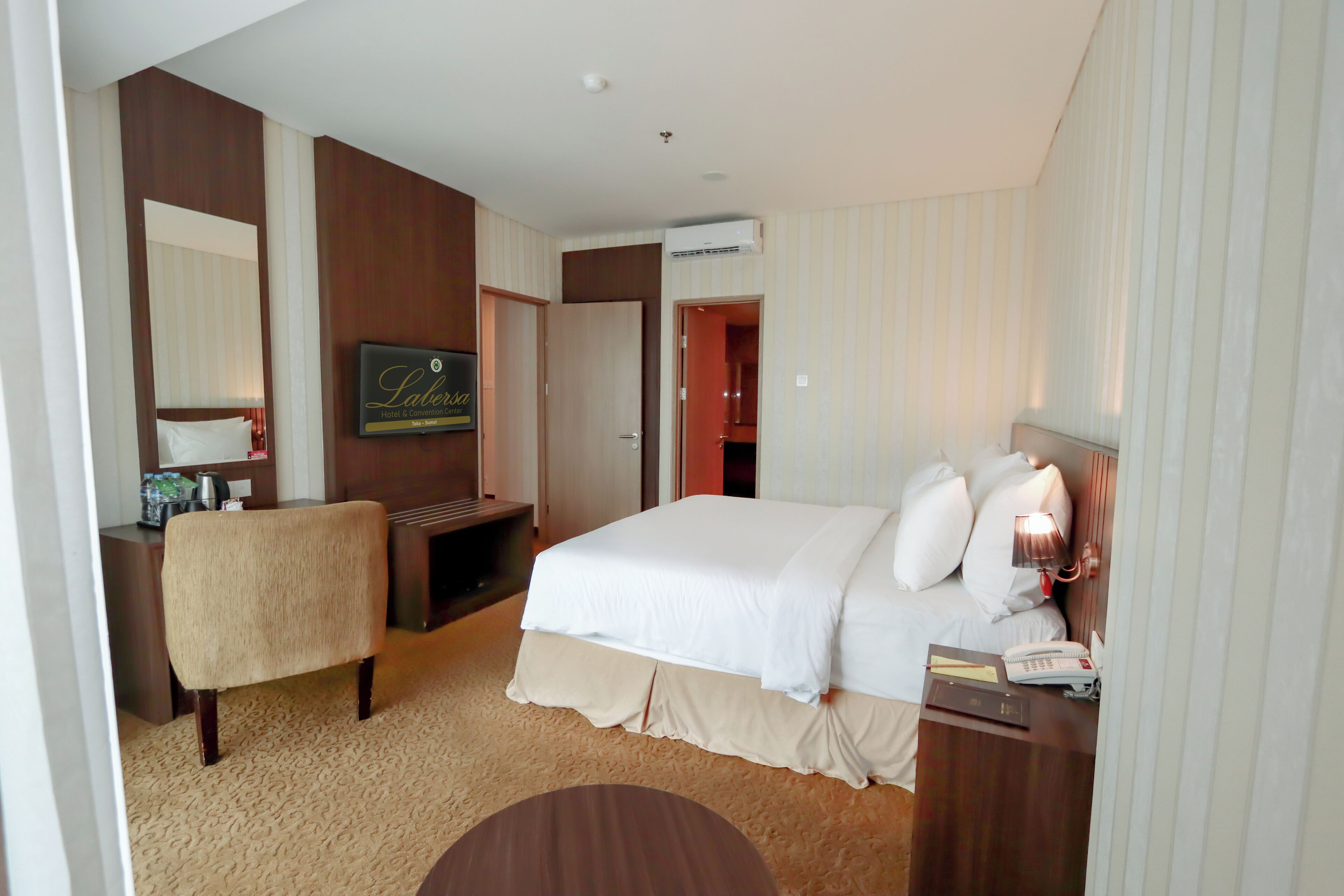 Ein Hotelzimmer mit Bett, Nachttisch, Lampe und Schreibtisch mit Stuhl.
