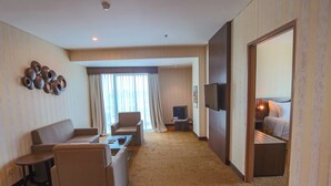 A hotel room with a sofa, armchair, small table, TV, and a bed with a nightstand. - Labersa Hotel And Convention Center Toba Balige (Balige)