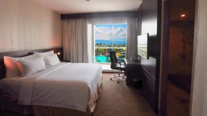 A hotel room with a large bed, a desk, a chair, and a TV. There is a window with a view of a pool and mountains. - Labersa Hotel And Convention Center Toba Balige (Balige)