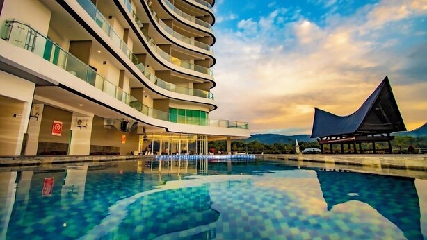 A modern hotel with a curved exterior, a pool, and a view of the mountains. - Labersa Hotel And Convention Center Toba Balige (Balige)