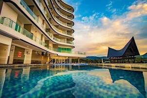 Um hotel moderno com fachada curva, piscina e vista para as montanhas.