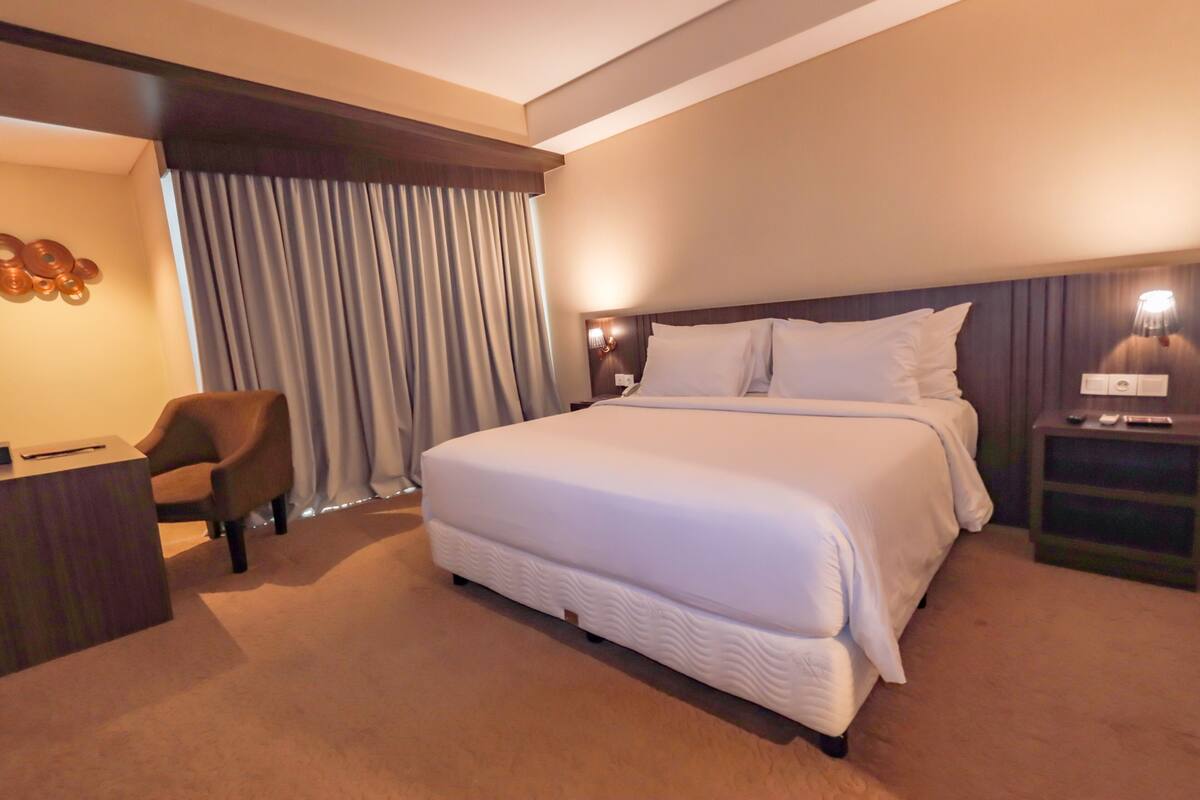 Une chambre d’hôtel avec un grand lit, un bureau, une chaise et une table de chevet avec une lampe.