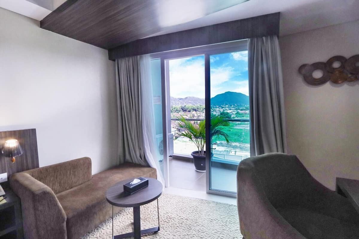 Une chambre d’hôtel moderne, dotée d’un canapé, d’une petite table et offrant une vue sur le paysage urbain grâce à de grandes fenêtres.