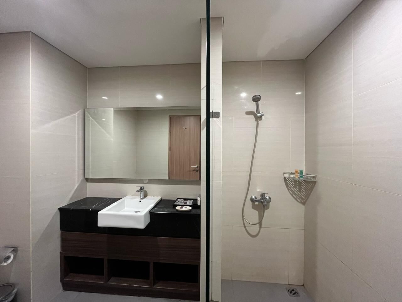 Un baño moderno con mampara de vidrio, lavamanos blanco, espejo y zona de ducha.