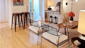 A modern living room with a wooden floor, a dining area with a table and chairs, a kitchen area with a stove, and a large window. - Alfama S Loft (Lisboa)