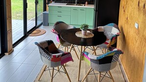 Eine moderne Küche mit Holzsärchen, ein Essbereich mit bunten Stühlen und ein großes Fenster mit Blick ins Freie.