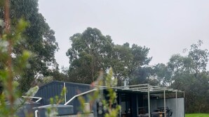 Une maison moderne dotée d’un espace extérieur couvert, entourée d’une pelouse bien entretenue et d’arbres.
