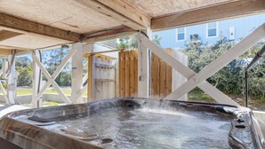 Un jacuzzi con terraza de madera y una vista a una casa azul al fondo.