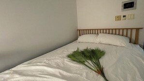 A single bed with white bedding and a wooden headboard. A bunch of green palm leaves is placed on the bed.