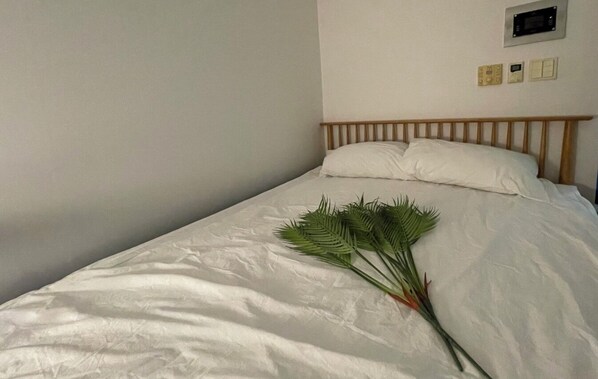 A single bed with white bedding and a wooden headboard. A bunch of green palm leaves is placed on the bed.