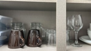 A shelf with various glassware, including two brown mugs and several clear glasses.