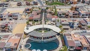 Eine Vogelperspektive zeigt ein Resort mit einem zentralen Pool, mehreren Gebäuden und einem Strandabschnitt.