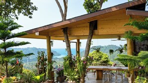 A covered outdoor area with a wooden table and chairs, surrounded by potted plants and trees. - Villa Bella Vista Samui (Koh Samui)