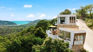 A modern two-story house with large windows, a stone facade, and a view of a coastal landscape. - Villa Bella Vista Samui (Koh Samui)