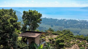 A wooden cabin with a sloped roof, surrounded by dense greenery and overlooking a coastal landscape. - Villa Bella Vista Samui (Koh Samui)