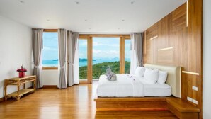 A spacious bedroom with a large bed, wooden flooring, and a view of the landscape through large windows. - Villa Bella Vista Samui (Koh Samui)