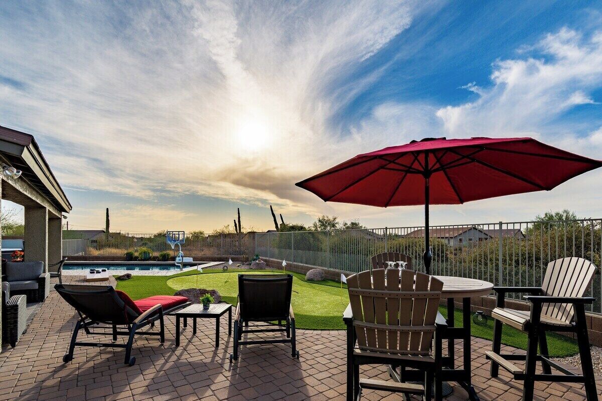 An outdoor patio with a pool, chairs, and a red umbrella.