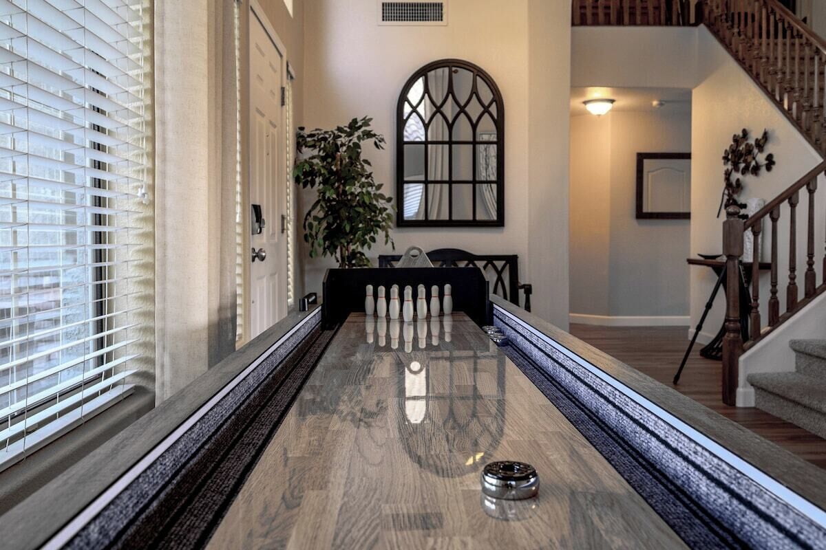 A bowling alley with a polished wooden floor, a pinsetter, and a single pin in the foreground.