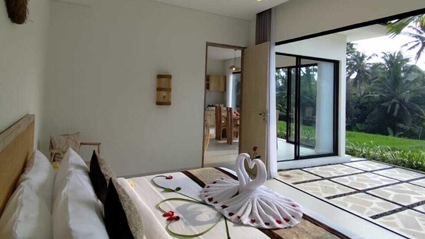 Een moderne slaapkamer met een groot bed, uitzicht op een weelderige tuin en een schuifdeur naar een terras.