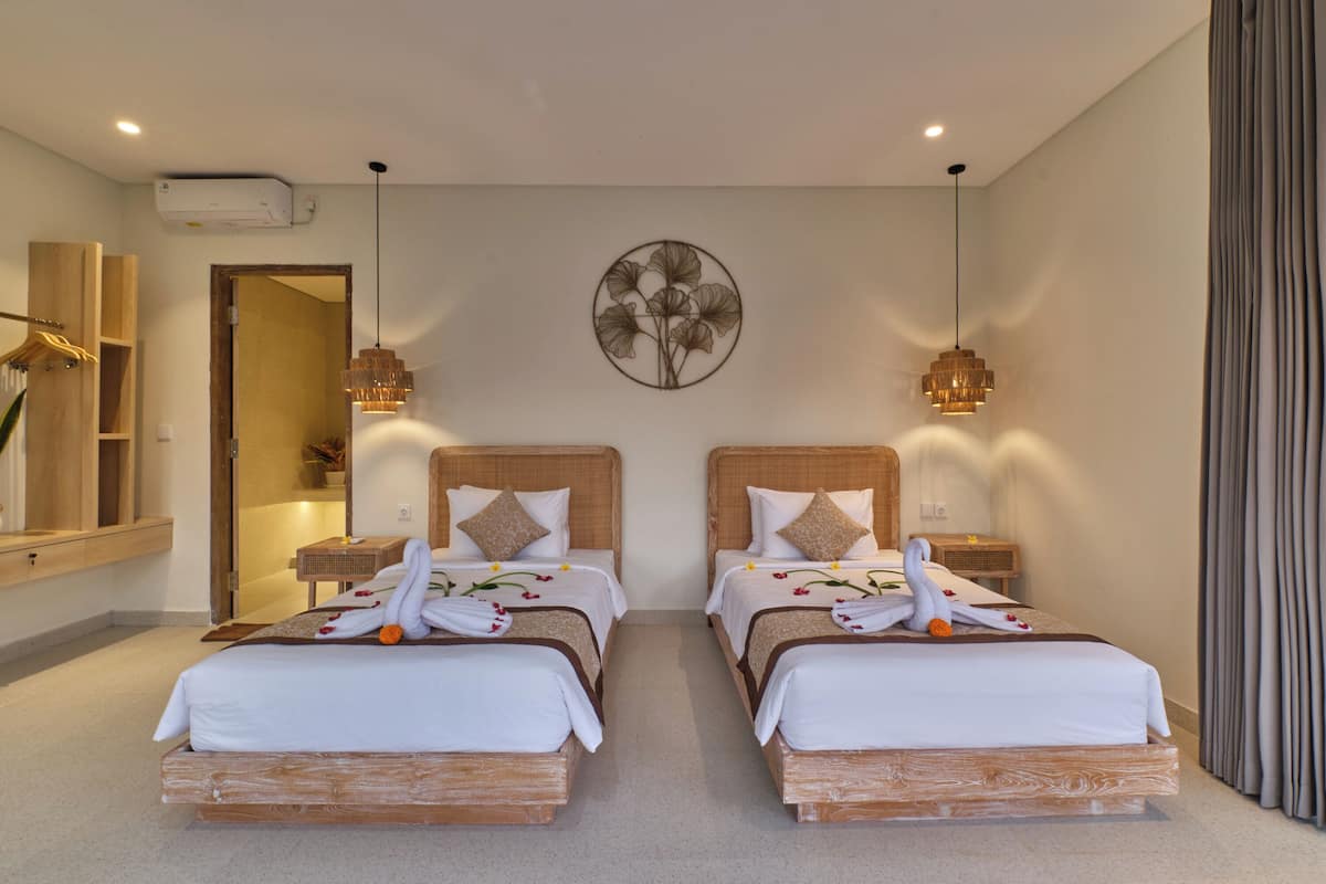 A hotel room with two beds, each with a wooden headboard, white bedding, and decorative swans. There are wall-mounted sconces and a large mirror.